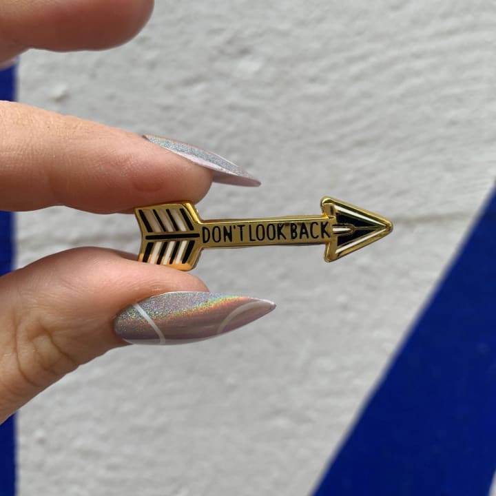 Don't Look Back Arrow Enamel Pin in Gold on Gift Card